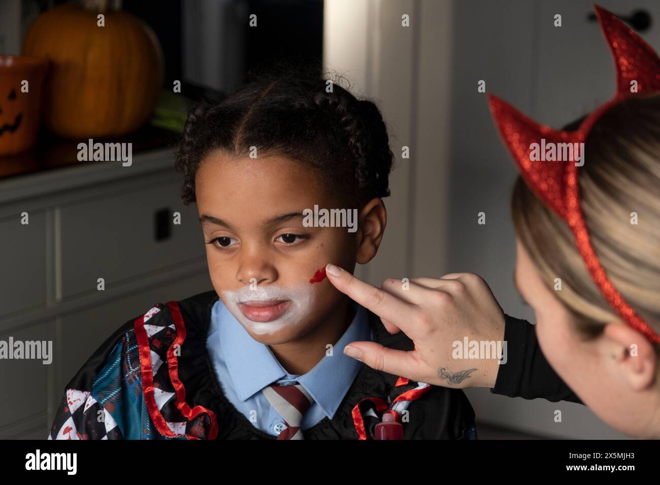 Primo piano di una donna che applica vernice rossa sulla faccia del figlio per Halloween Foto Stock