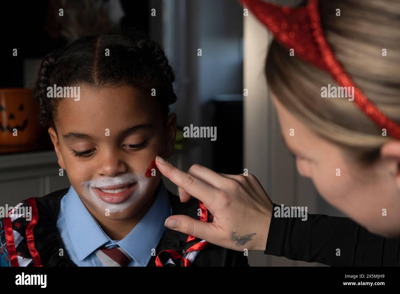 Primo piano di una donna che applica vernice rossa sulla faccia dei figli per Halloween Foto Stock