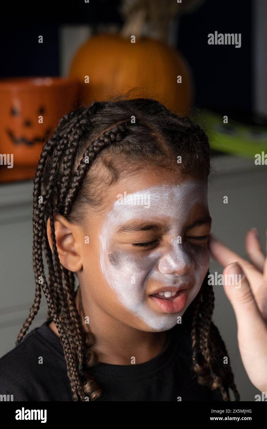 Primo piano di una donna che applica la pittura sulla faccia dei figli per Halloween Foto Stock