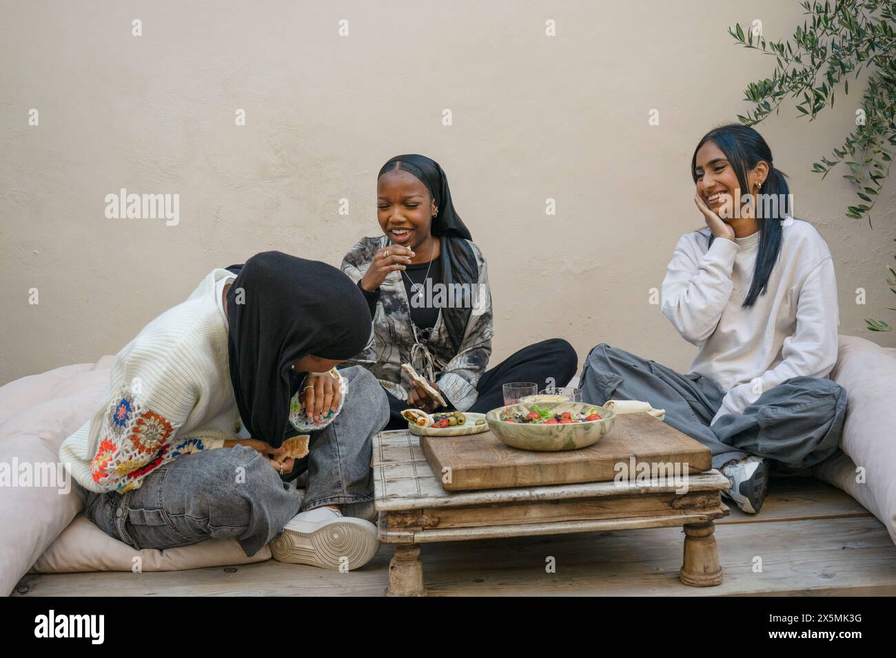 Amici che indossano hijab e si godono spuntini sul patio Foto Stock