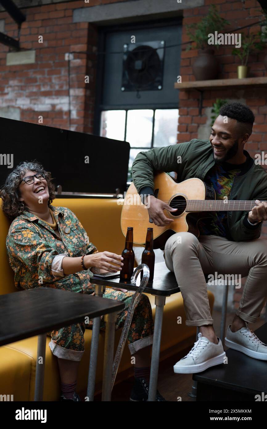 Giovane che suona la chitarra acustica nella sala d'ufficio, donna che ride Foto Stock