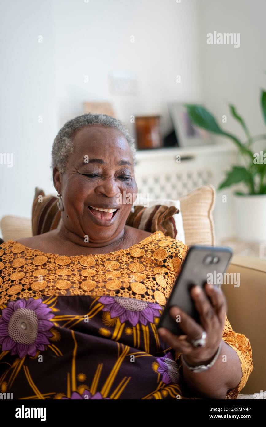 Donna anziana sorridente che ha una videochiamata sullo smartphone a casa Foto Stock