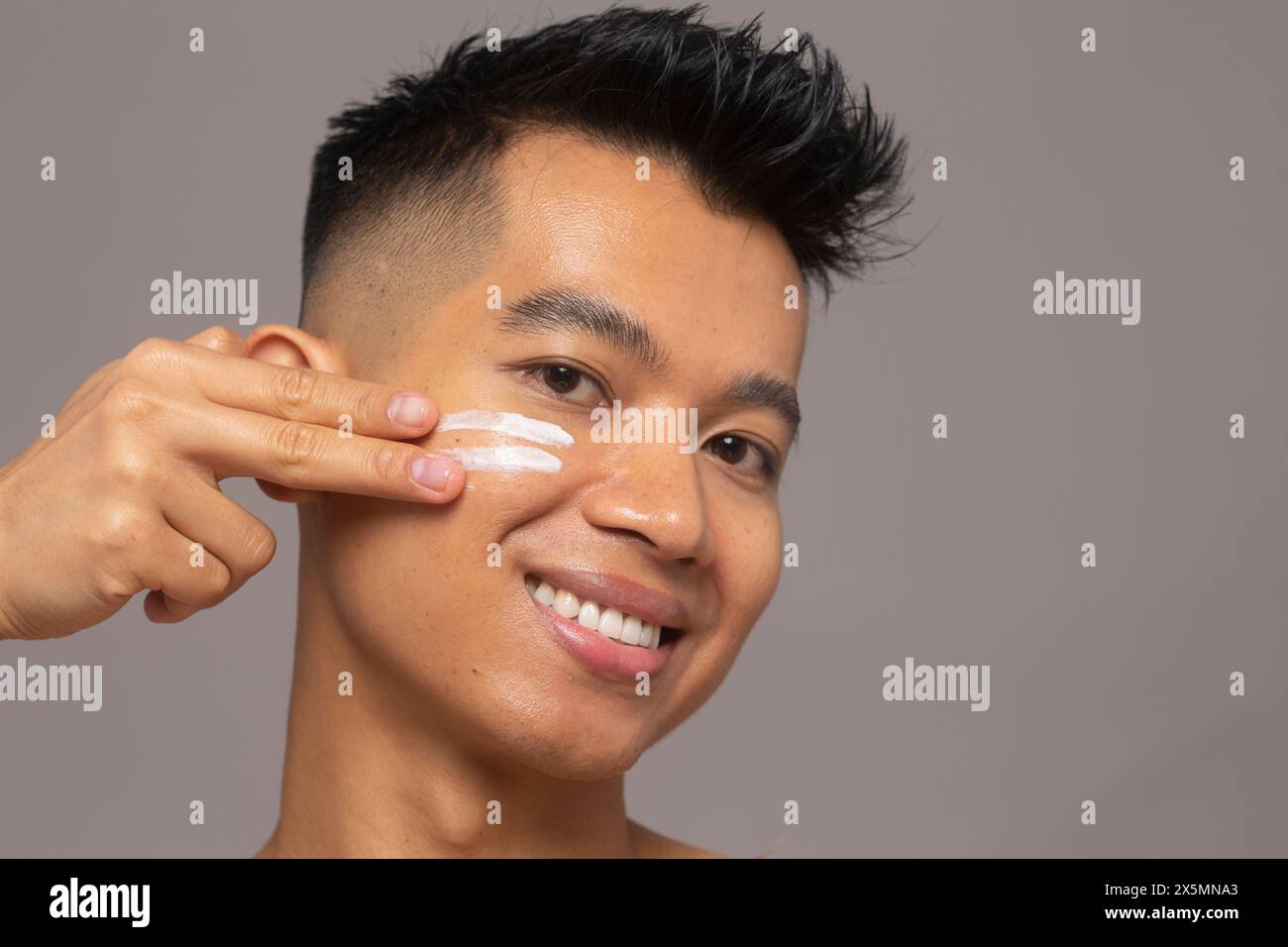Ritratto in studio di una persona sorridente che applica idratante sul viso Foto Stock