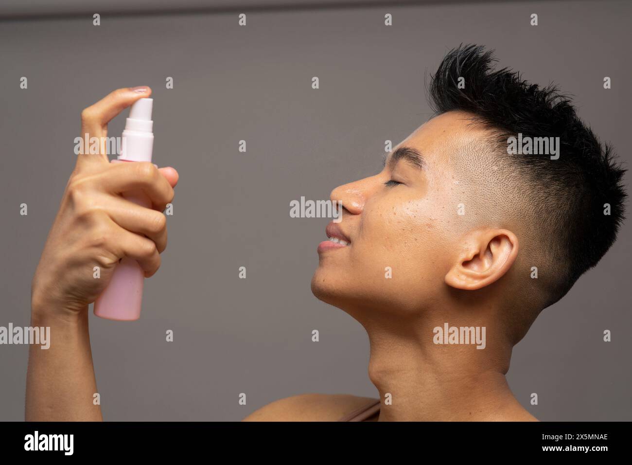 Profilo della persona che spruzza nebbia sul viso Foto Stock
