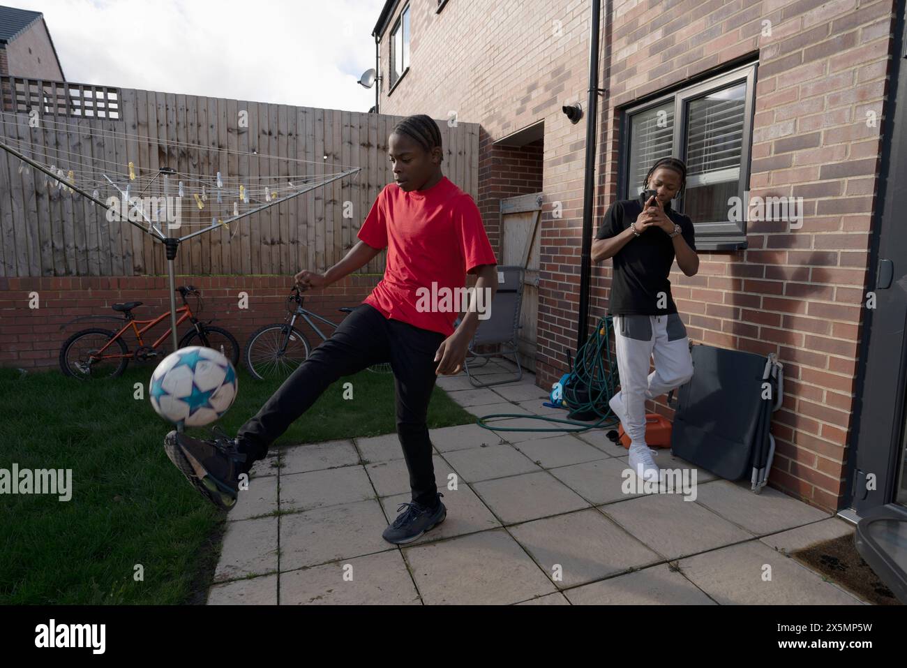 Ragazzo adolescente?fotografare un amico che gioca a calcio nel cortile posteriore Foto Stock