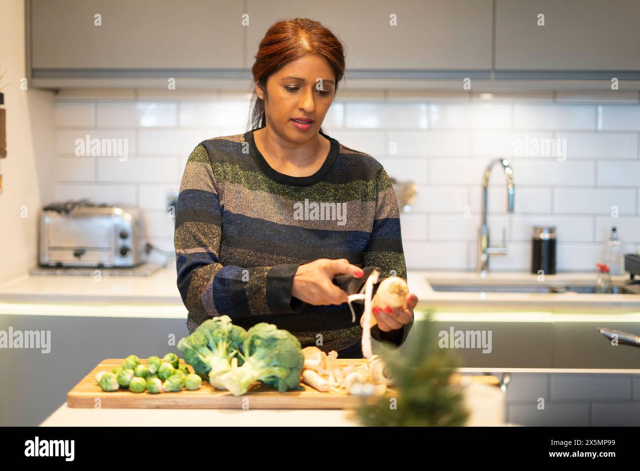Donna che sbuccia la radice di prezzemolo in cucina Foto Stock