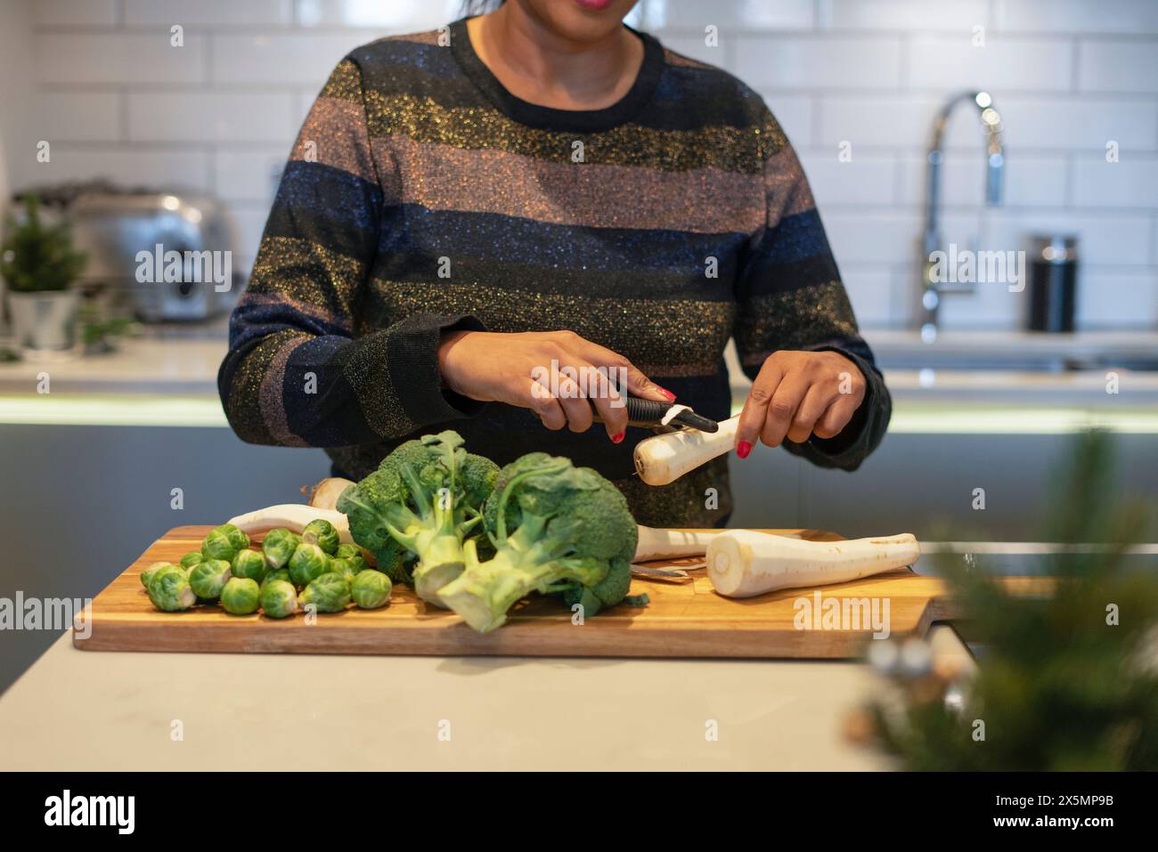 Sezione intermedia di donna che sbuccia la radice di prezzemolo in cucina Foto Stock