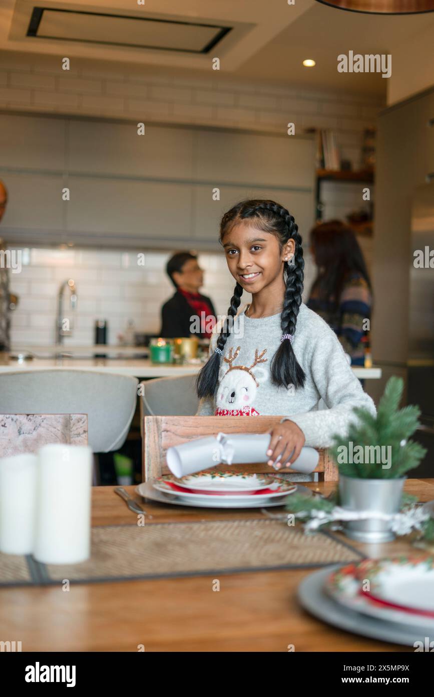 Ragazza che mette il cracker di Natale sul tavolo, madre e nonna sullo sfondo Foto Stock