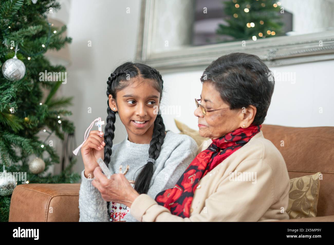 Ragazza con nonna che tiene in mano perline rosarie e croce all'albero di Natale Foto Stock