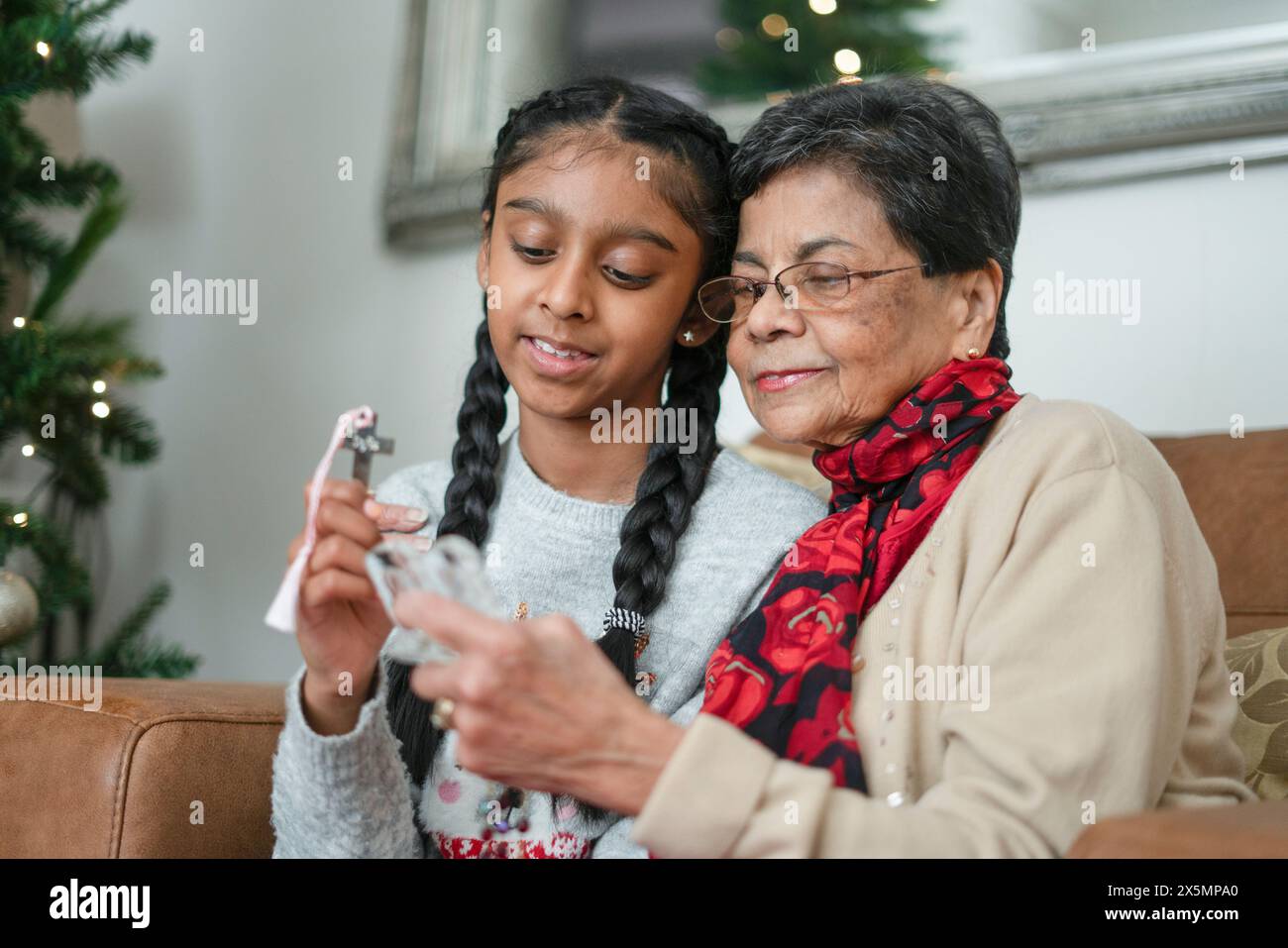 Ragazza con nonna che tiene la croce all'albero di Natale Foto Stock