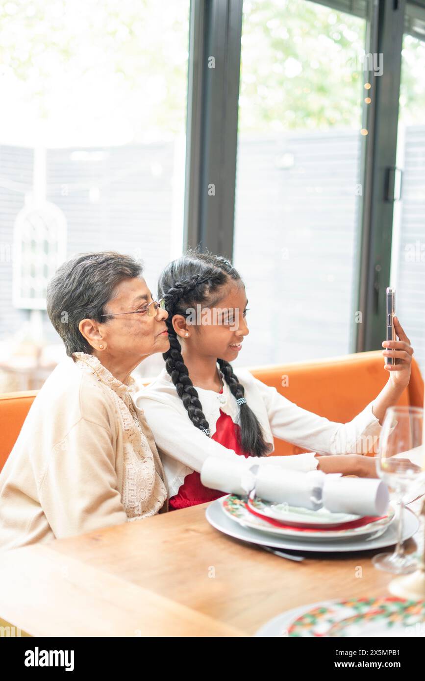 Ragazza sorridente con nonna che si fa selfie a tavola Foto Stock