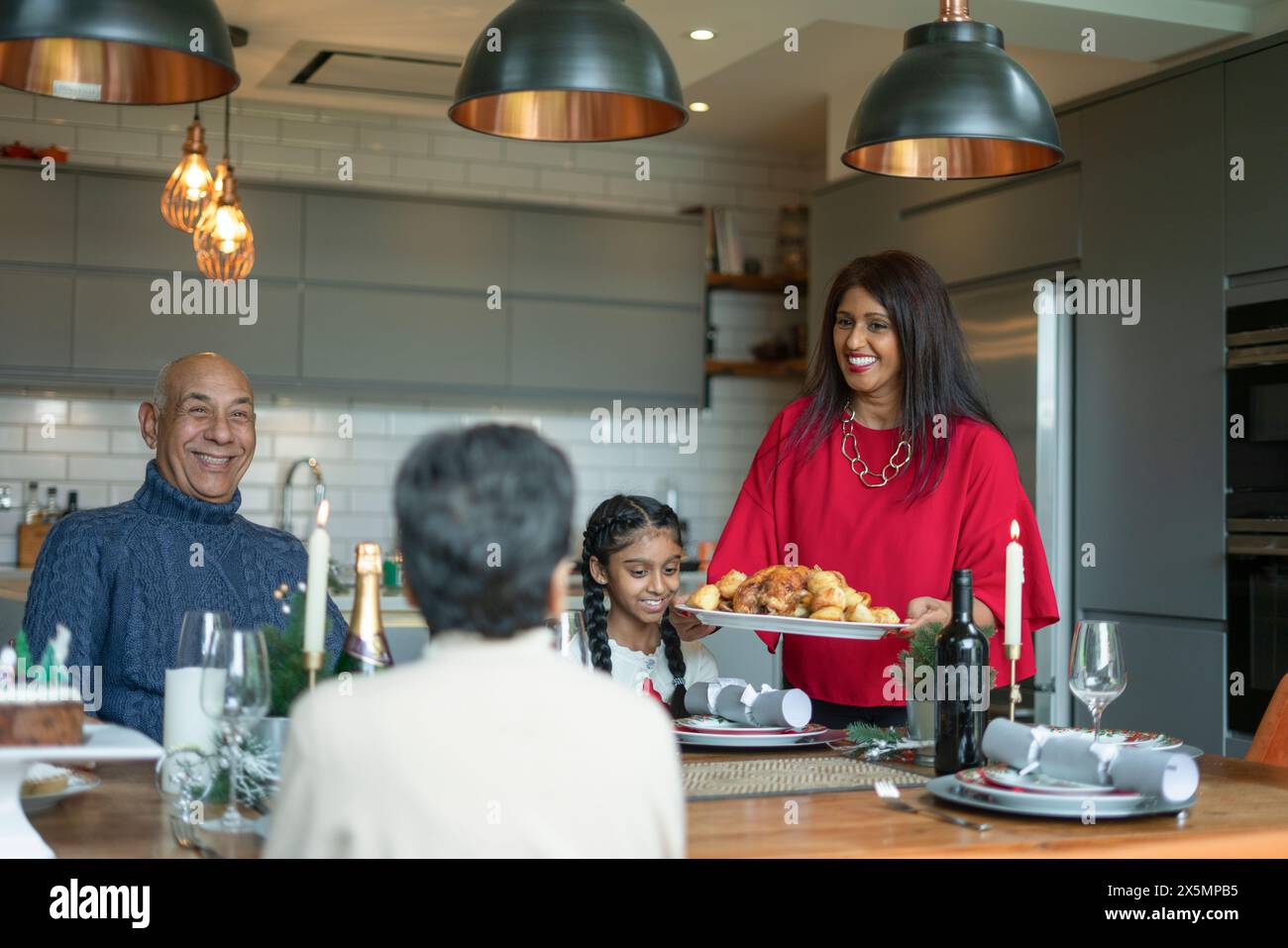 Donna sorridente che serve tacchino arrosto alla famiglia a tavola Foto Stock