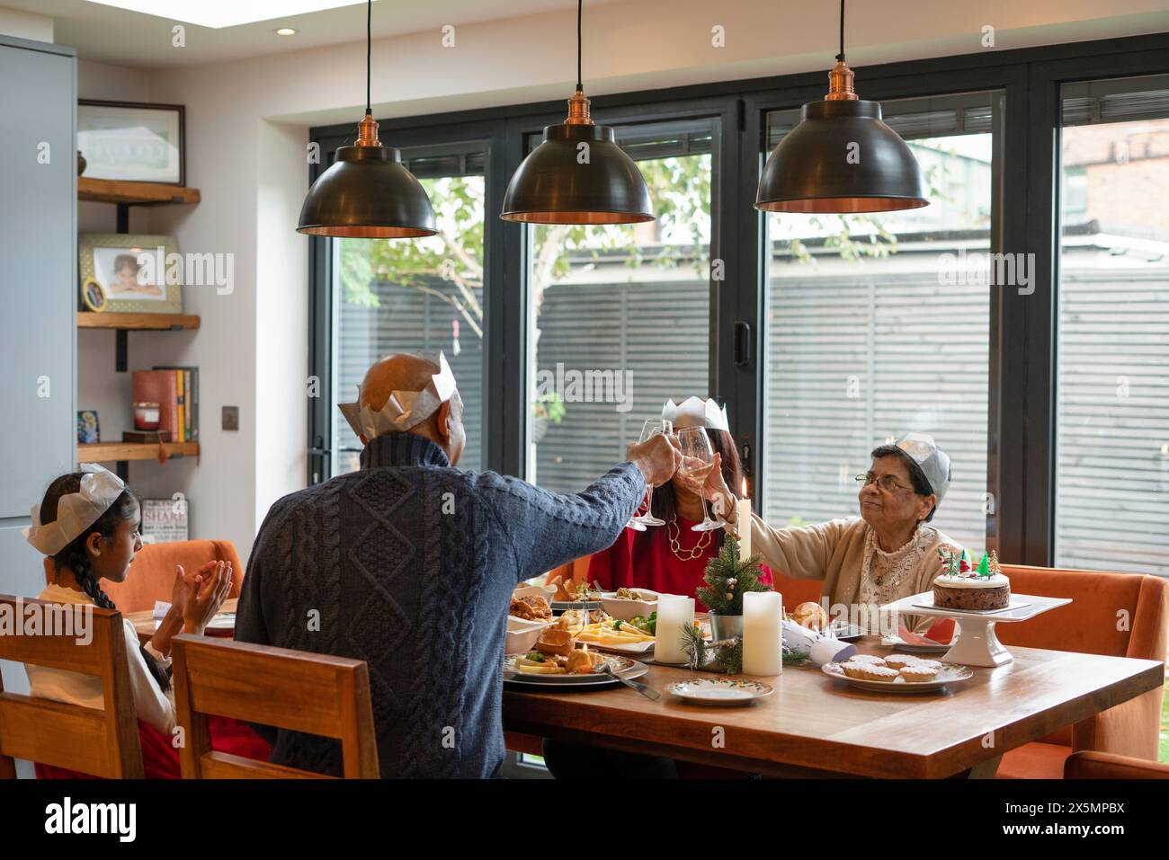 Famiglia che indossa corone di carta per brindare durante la cena di Natale Foto Stock