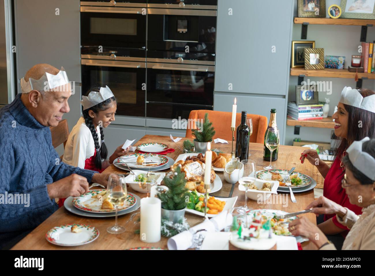 La famiglia indossa corone di carta e si gode la cena di Natale Foto Stock