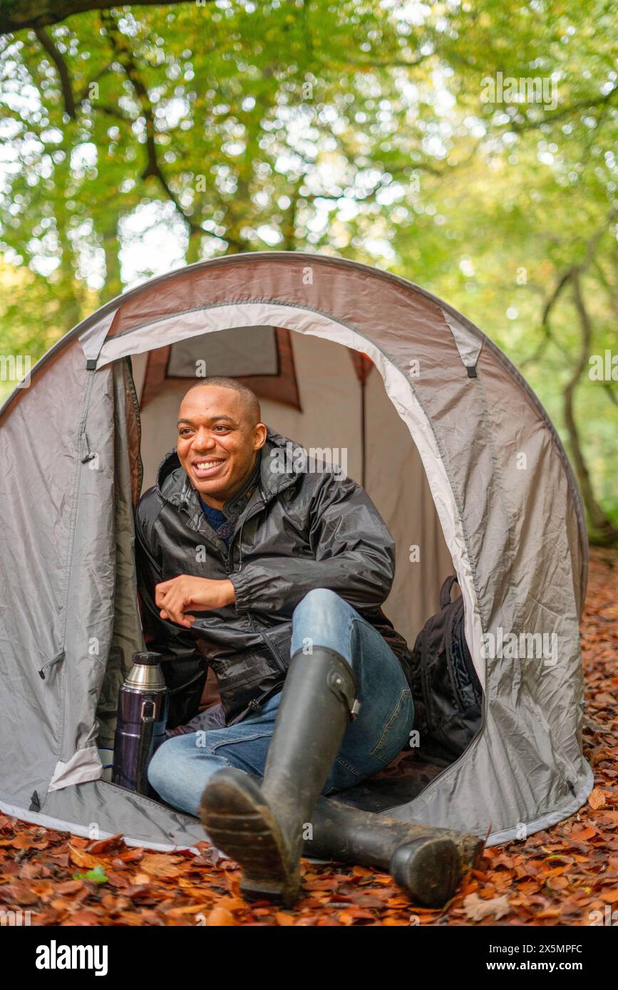 Uomo sorridente seduto in tenda nella foresta Foto Stock