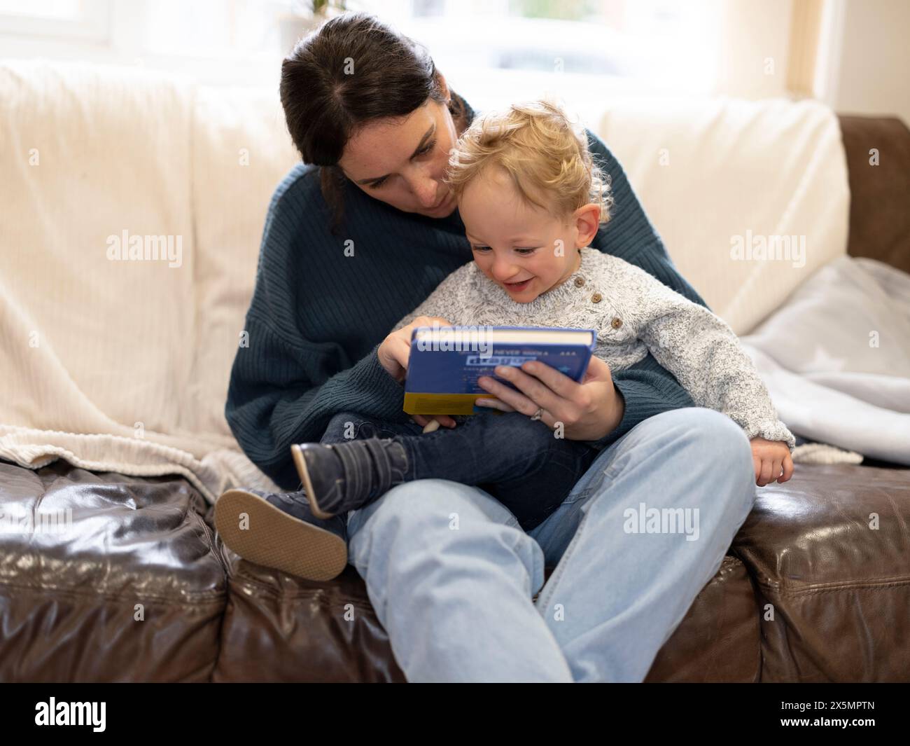 Madre che legge al sole a casa Foto Stock