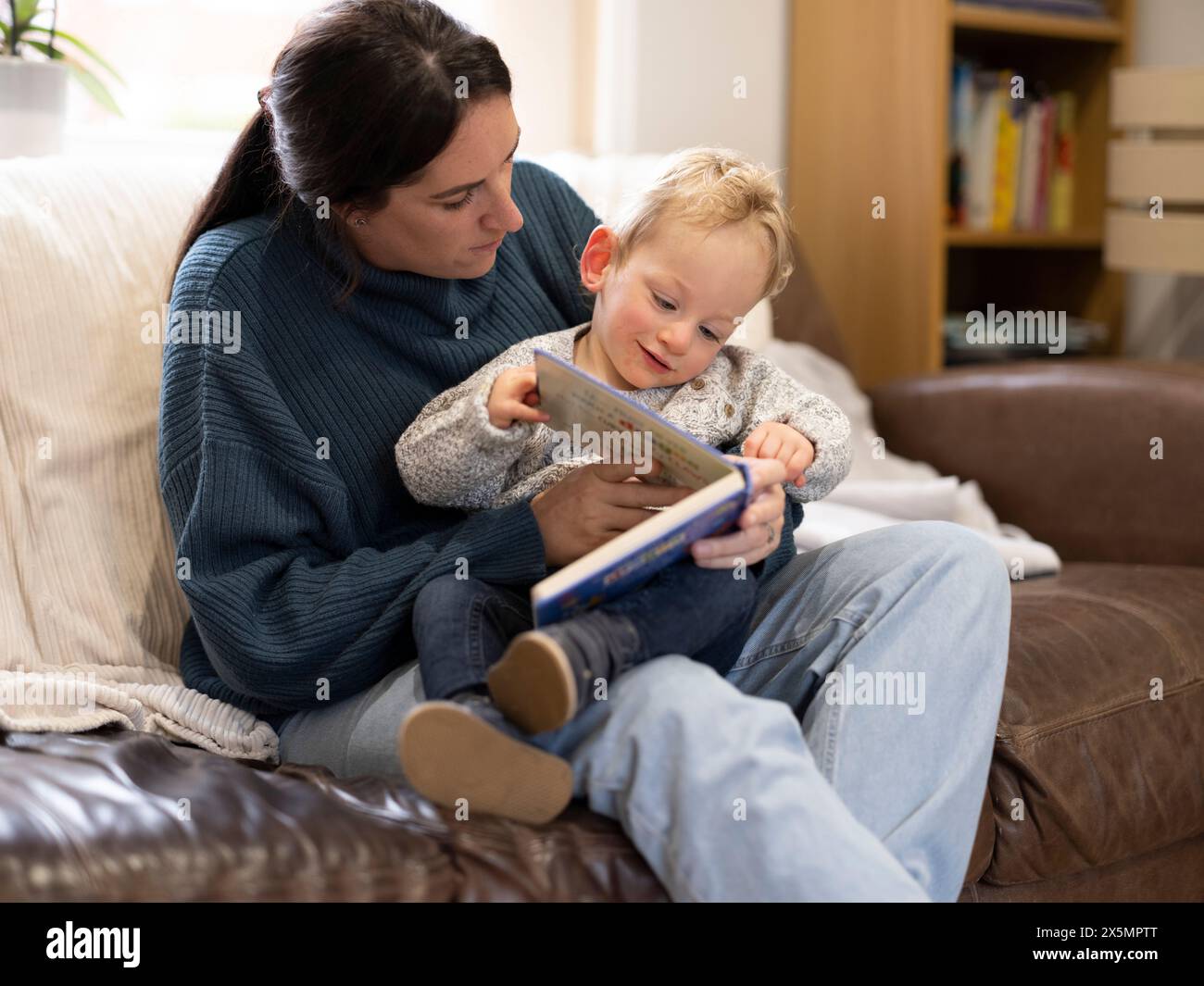 Ragazzo seduto in braccio alla madre e guardando il libro Foto Stock