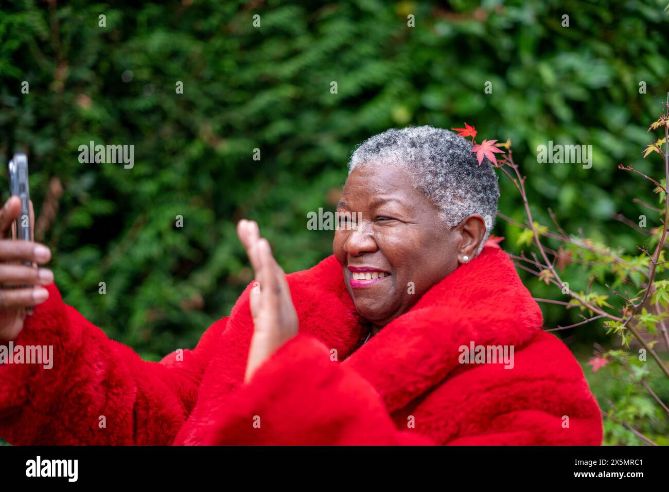 Donna anziana che indossa un cappotto di pelliccia rossa e usa il telefono Foto Stock