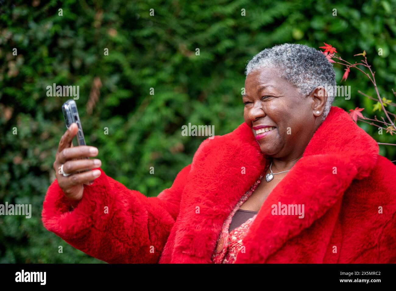 Donna anziana che indossa un cappotto di pelliccia rossa e usa il telefono Foto Stock