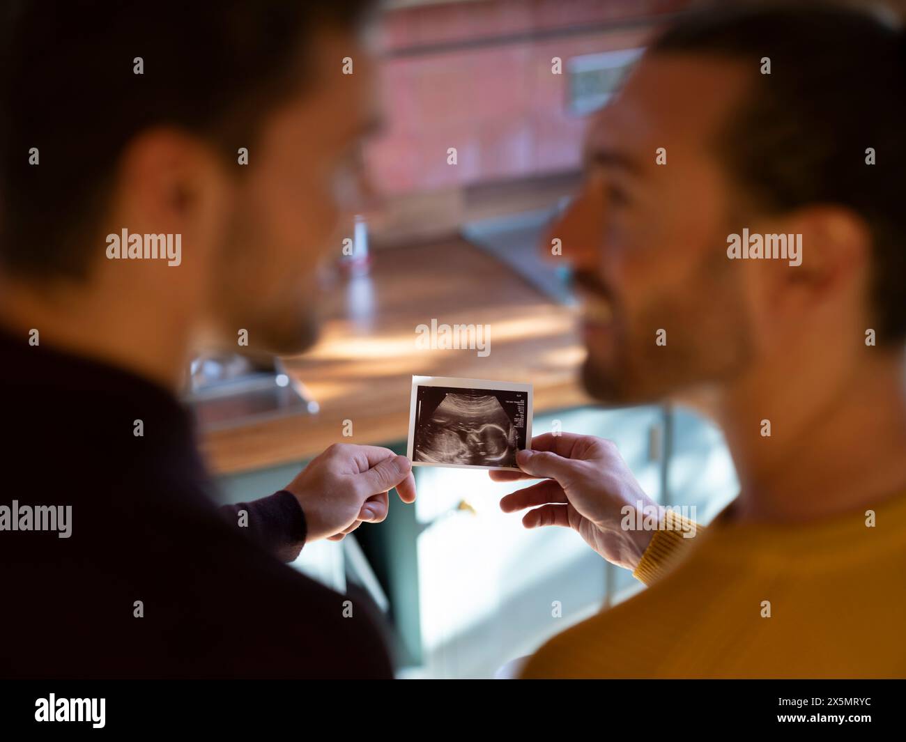 Coppia gay che tiene una scansione a ultrasuoni del bambino Foto Stock