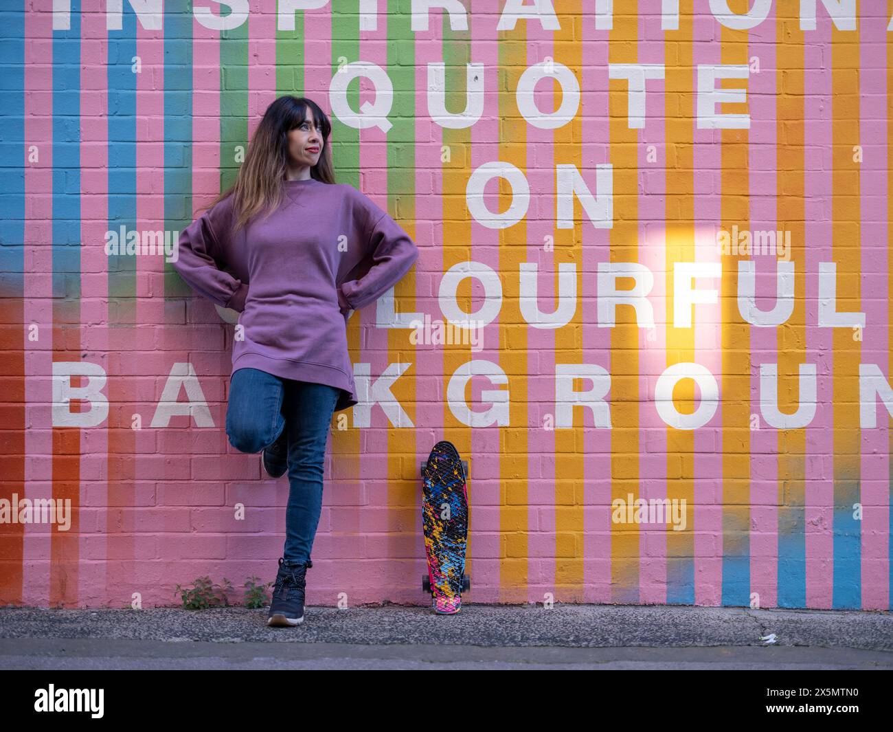 Ritratto di donna con skateboard contro pareti di mattoni colorati Foto Stock