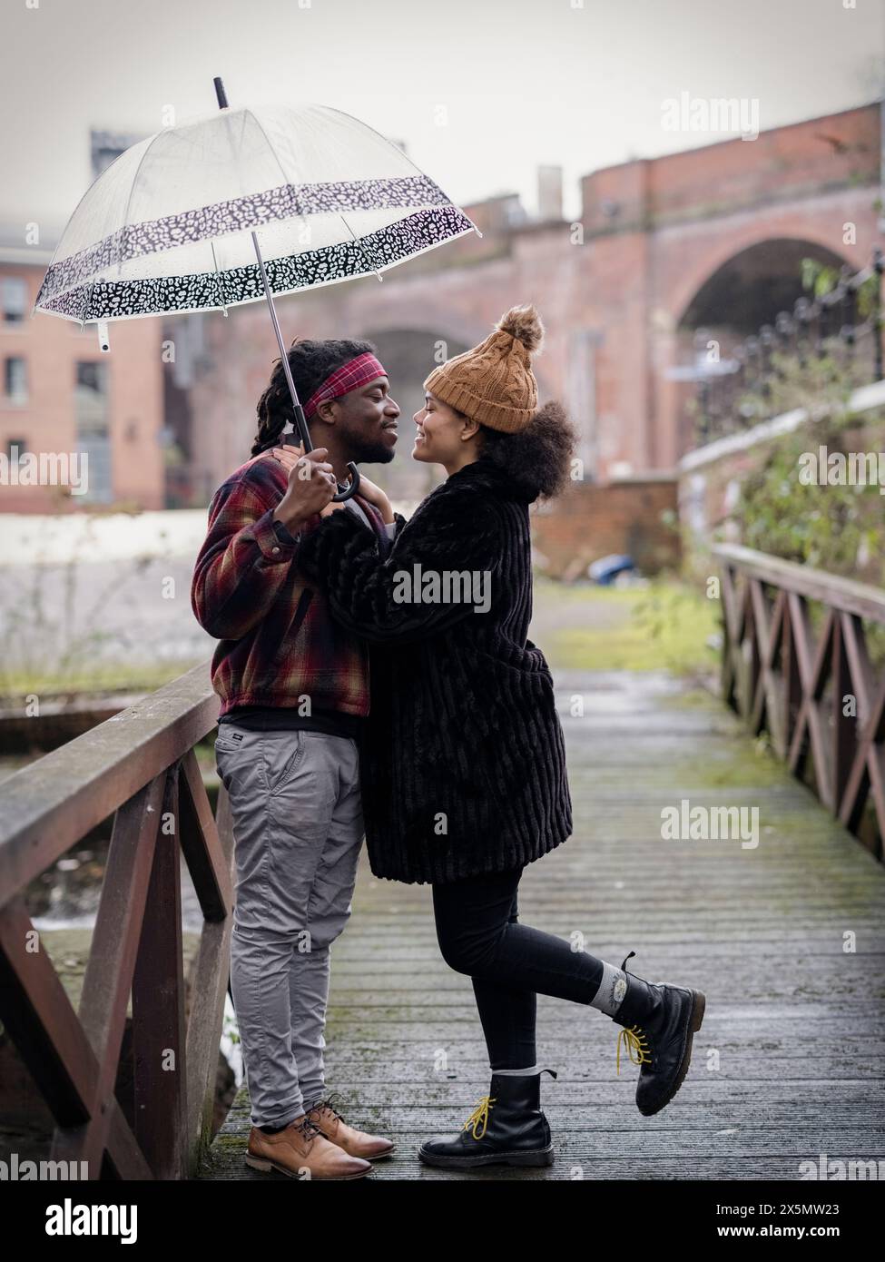 Coppia con ombrello in piedi faccia a faccia sulla passerella Foto Stock
