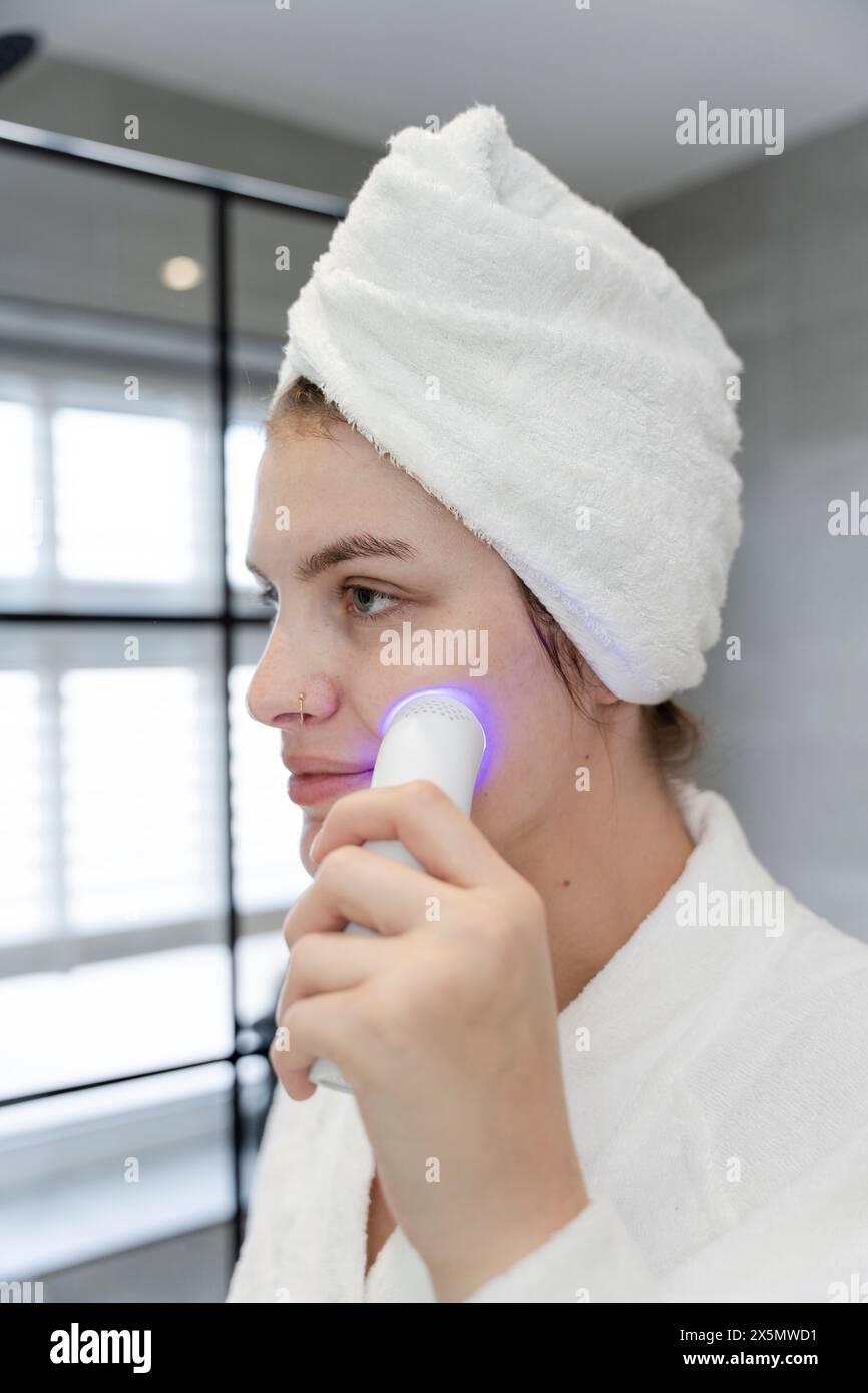 Donna con asciugamano turbante che fa terapia con luce blu sul viso Foto Stock