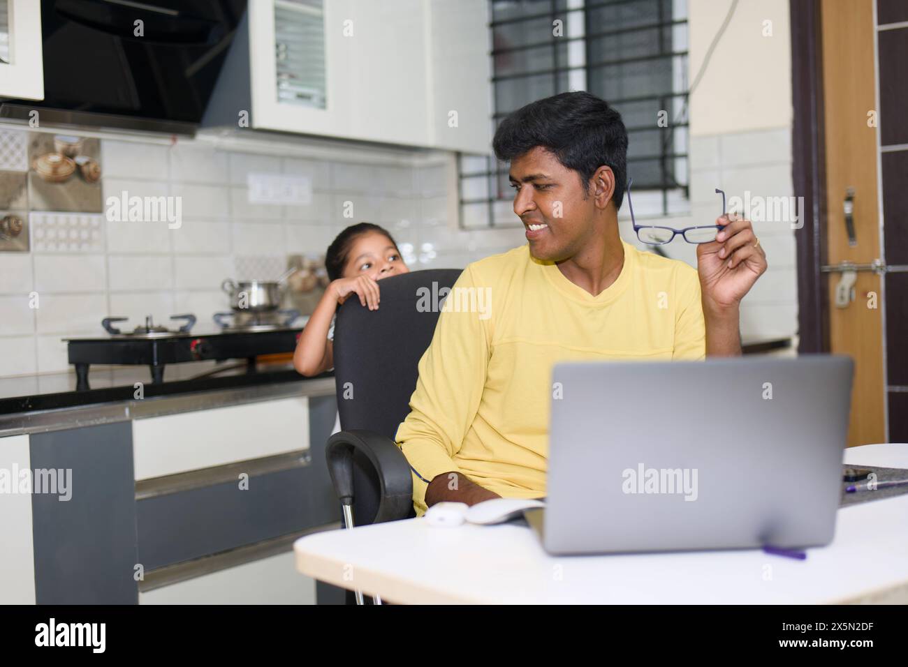 Un padre indiano premuroso guida pazientemente la sua giovane figlia mentre usa un computer portatile al loro tavolo da cucina. Foto Stock