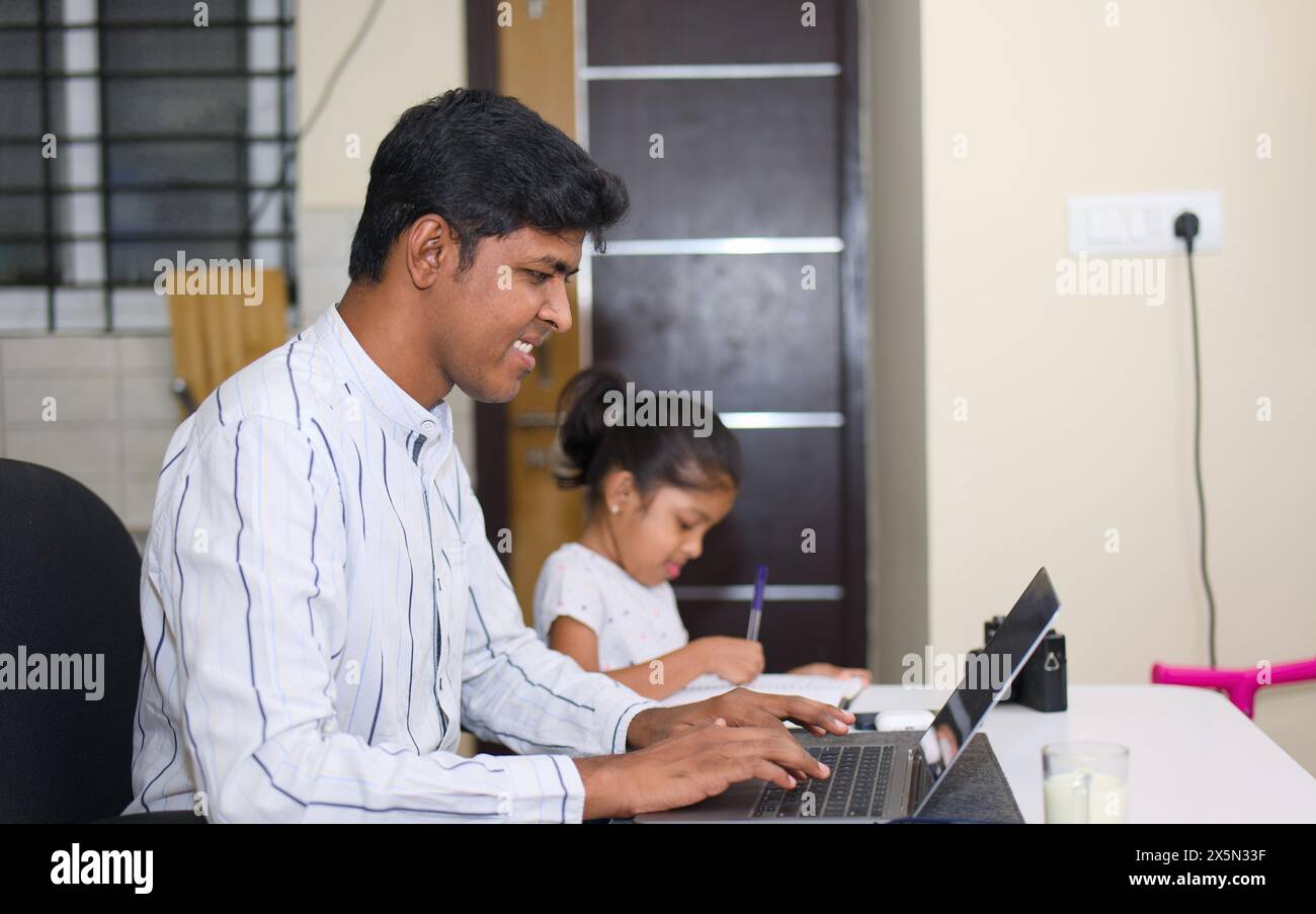 Un padre indiano sorride mentre aiuta pazientemente la sua figlia a imparare a usare un computer portatile sul divano nel loro salotto illuminato. Foto Stock