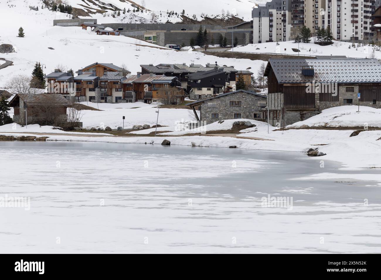 Gli alloggi nel quartiere Val Claret della stazione sciistica alpina francese di Tignes sono vuoti in bassa stagione, mentre il lago ghiacciato inizia a scongelarsi in primavera. Foto Stock