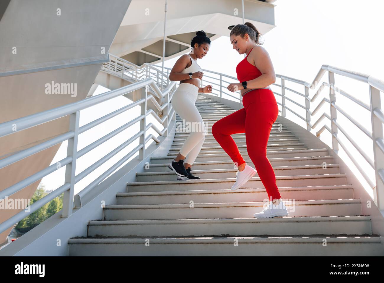 Due giovani femmine con diversi tipi di corpo che si allenano insieme all'aperto. Lunghezza completa di due donne che fanno un allenamento. Foto Stock