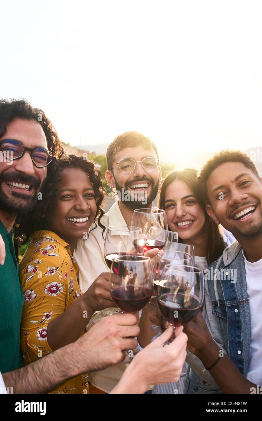 Gruppo di amici multirazziali che brinda vino rosso e festeggia la festa estiva in casa di campagna. Foto Stock