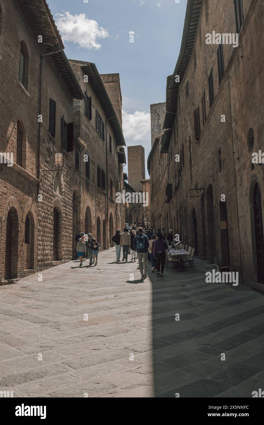 Turisti che camminano lungo una strada trafficata nel centro della storica città medievale di San Gimignano in Toscana, Italia, in una bella giornata di sole. Foto Stock