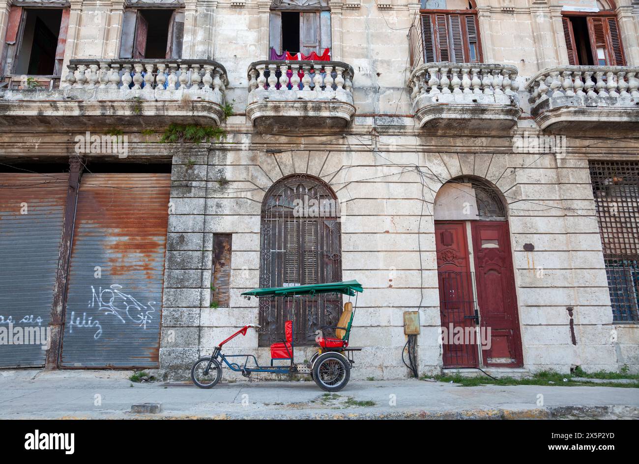 Taxi a pedali parcheggiato fuori dall'edificio fatiscente nel centro di Havana, Cuba Foto Stock