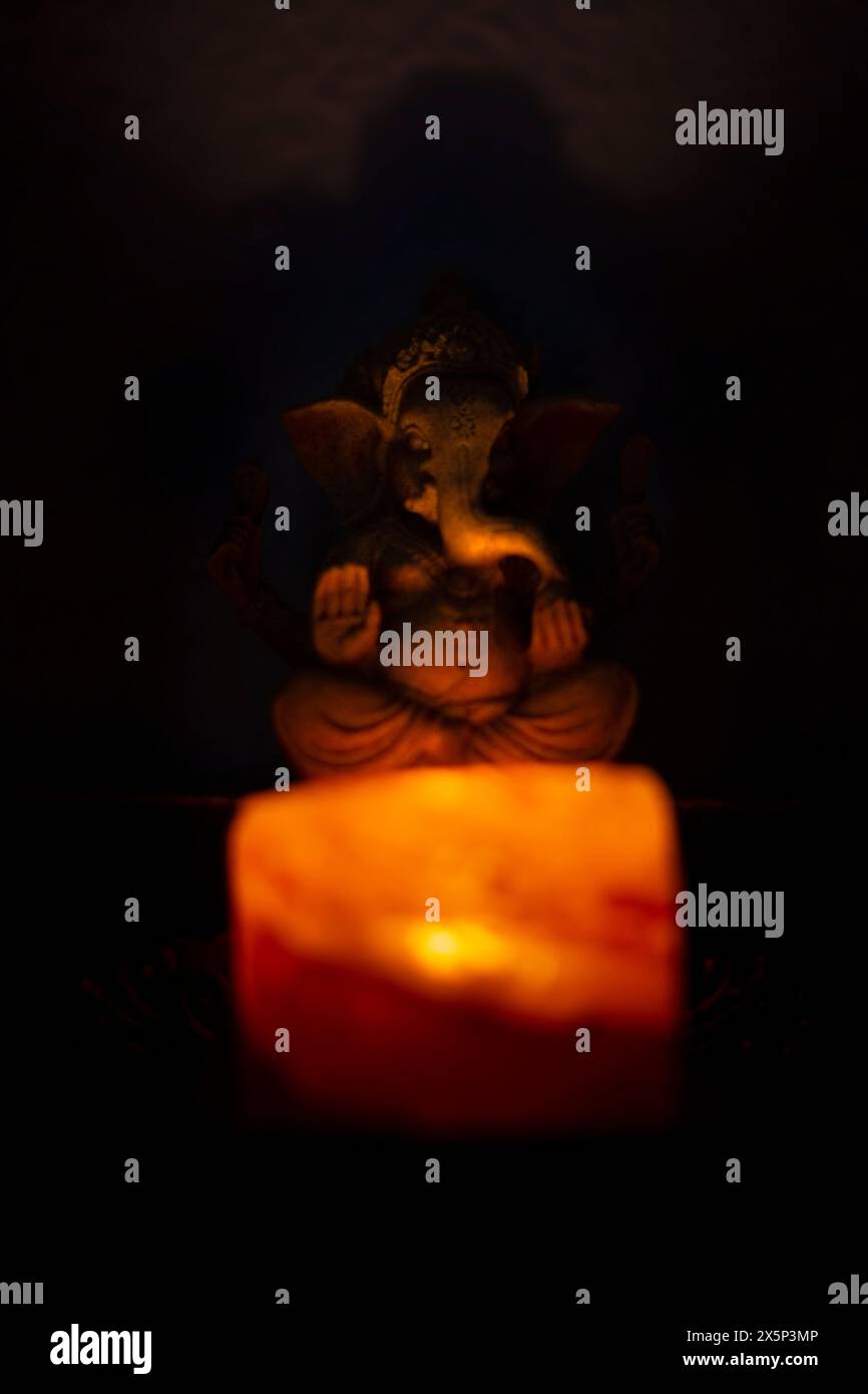 Figura della dea Ganesha dietro un portacandele con la luce arancione della candela. Messa a fuoco selettiva Foto Stock