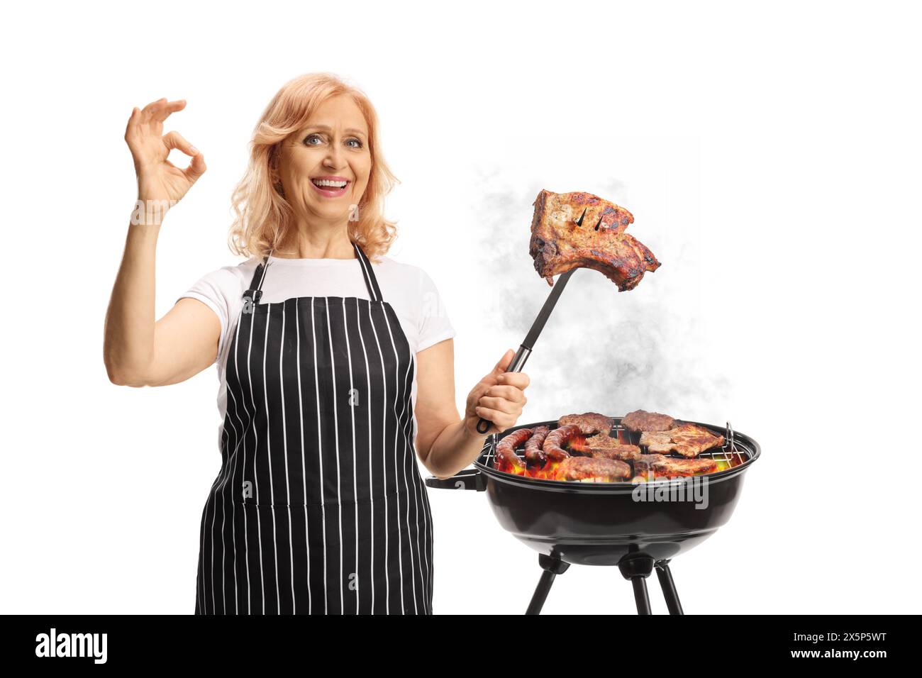 Donna che grigia la carne su un barbecue e tiene in mano una bistecca con una forchetta isolata su sfondo bianco Foto Stock