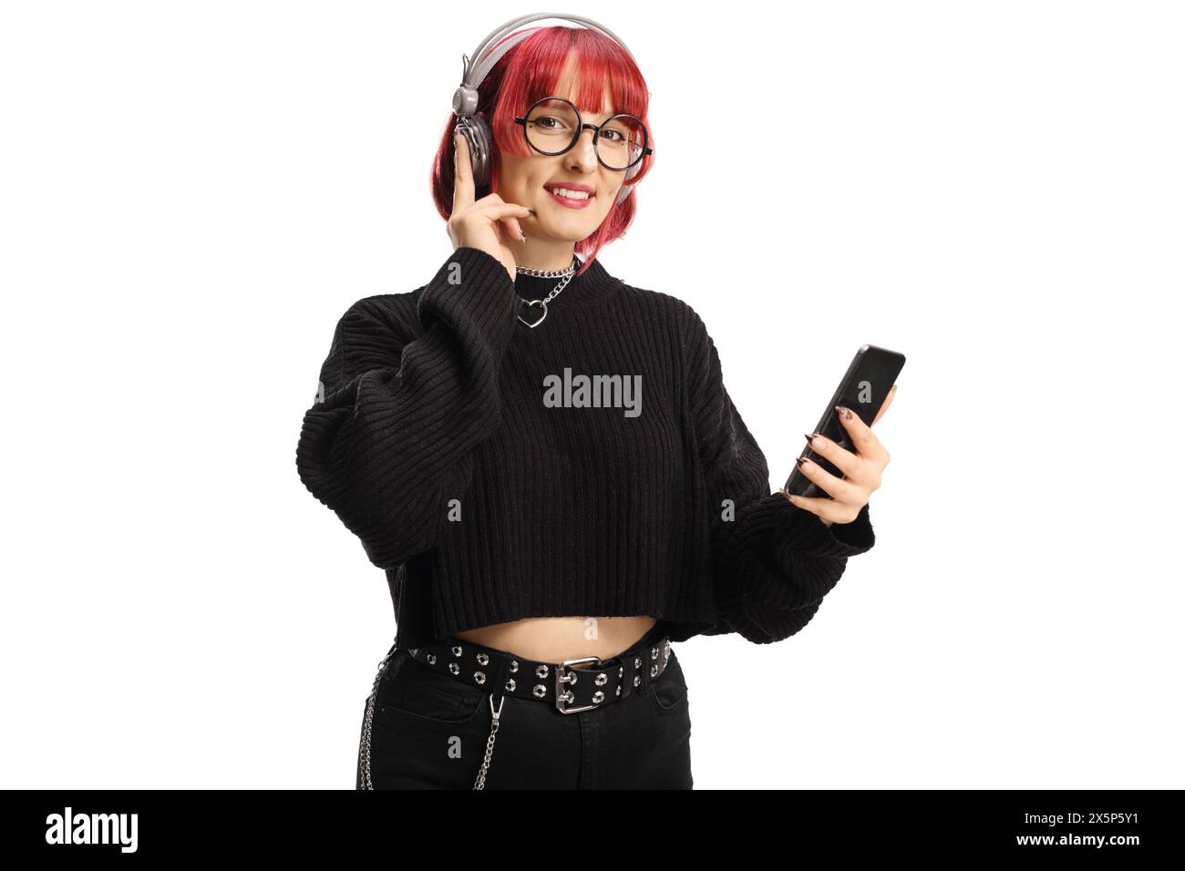 Giovane donna alla moda con capelli rossi che ascolta la musica con le cuffie e lo smartphone isolato su sfondo bianco Foto Stock