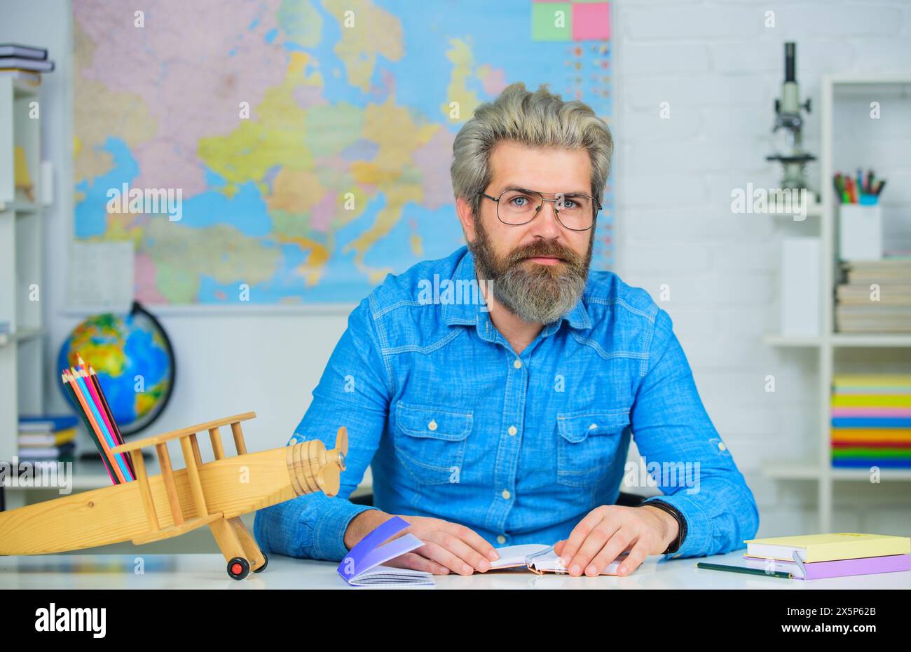 Un insegnante di sesso maschile fa l'esame all'università. Studentessa barba con occhiali e camicia in denim seduta alla scrivania in classe. Prova della conoscenza. Studiando per Foto Stock