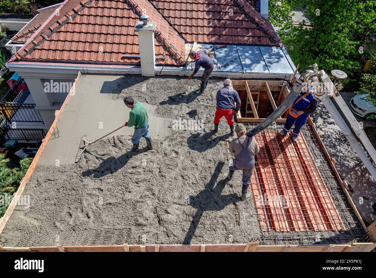 Gli operai edili versano la miscela di calcestruzzo su una lastra del tetto in acciaio rinforzato. Foto Stock