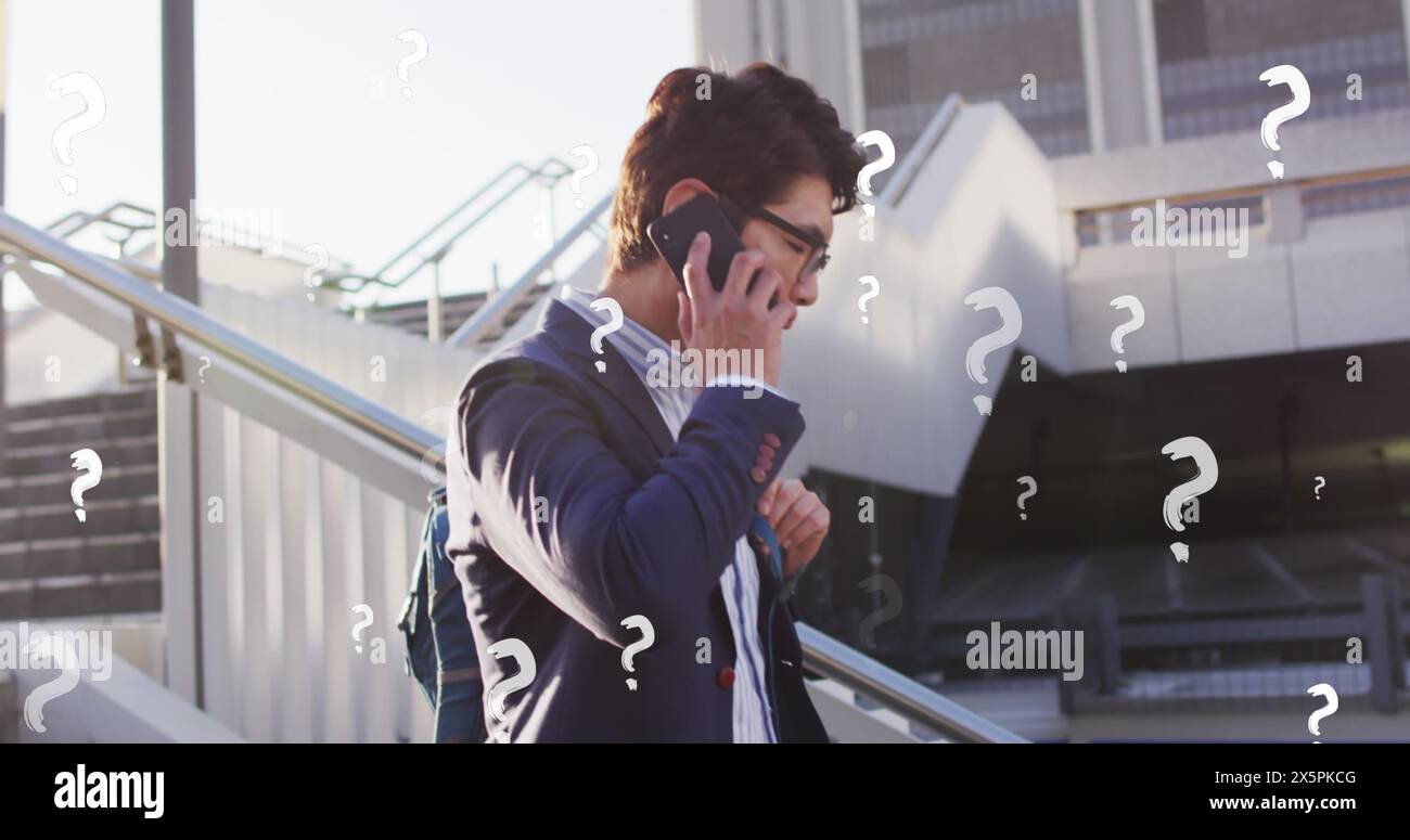 Immagine di punti interrogativi sull'uomo d'affari asiatico che parla al cellulare mentre si muove giù per i gradini Foto Stock