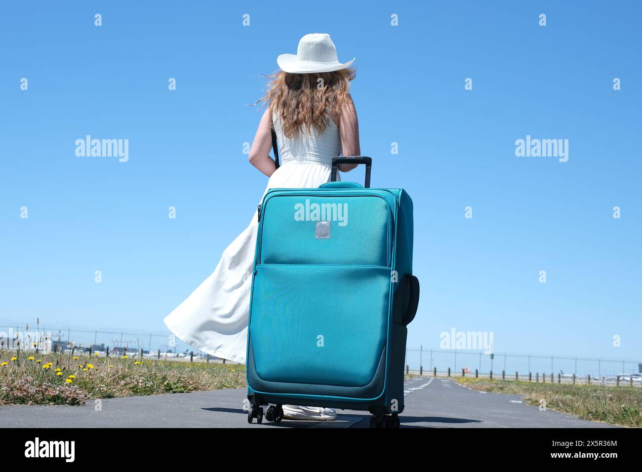 Le gambe di donna da vicino camminano su strada asfaltata e viaggiano con la valigia da viaggio . Autostop femminile in giro per il paese. Una giovane ragazza con un abito bianco e un cappello enorme con valigia viaggia in tutto il mondo Foto Stock