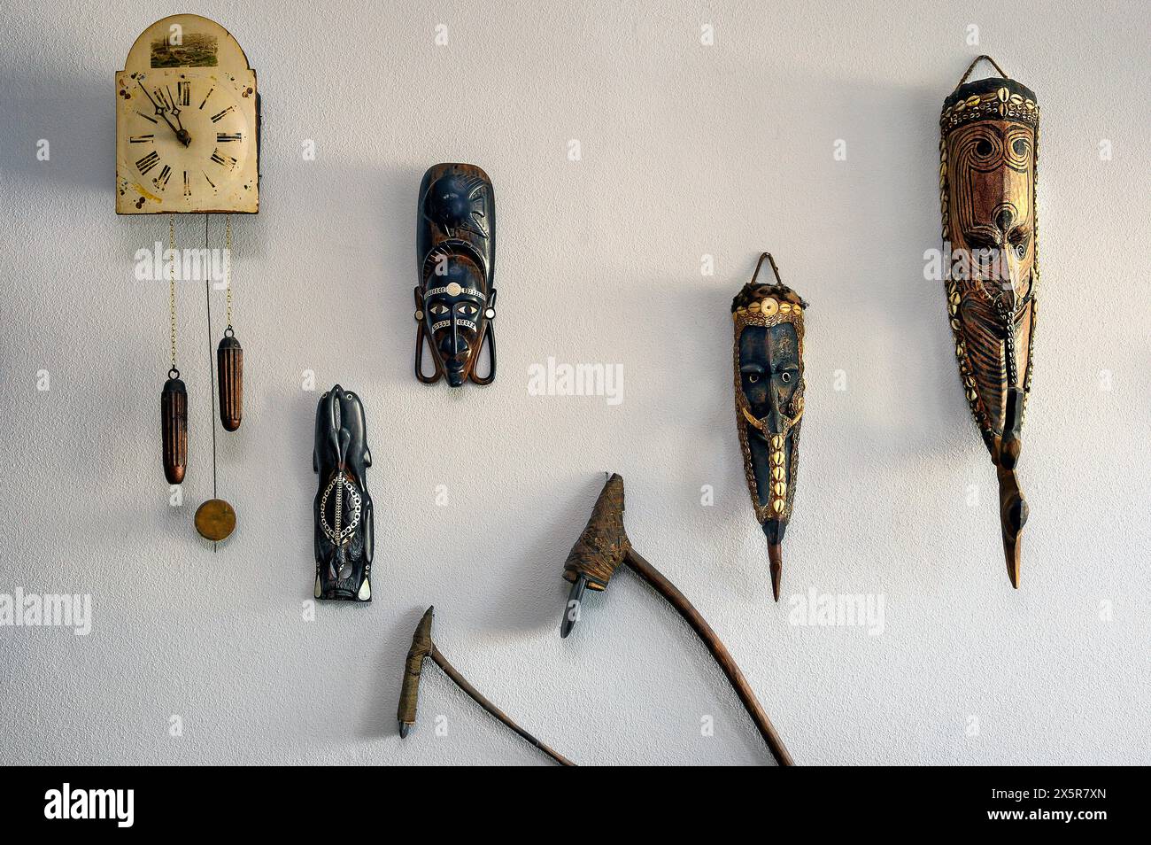 Decorazioni murali con vecchio orologio a pendolo e maschere da Papua nuova Guinea, Allgaeu, Svevia, Baviera, Germania Foto Stock