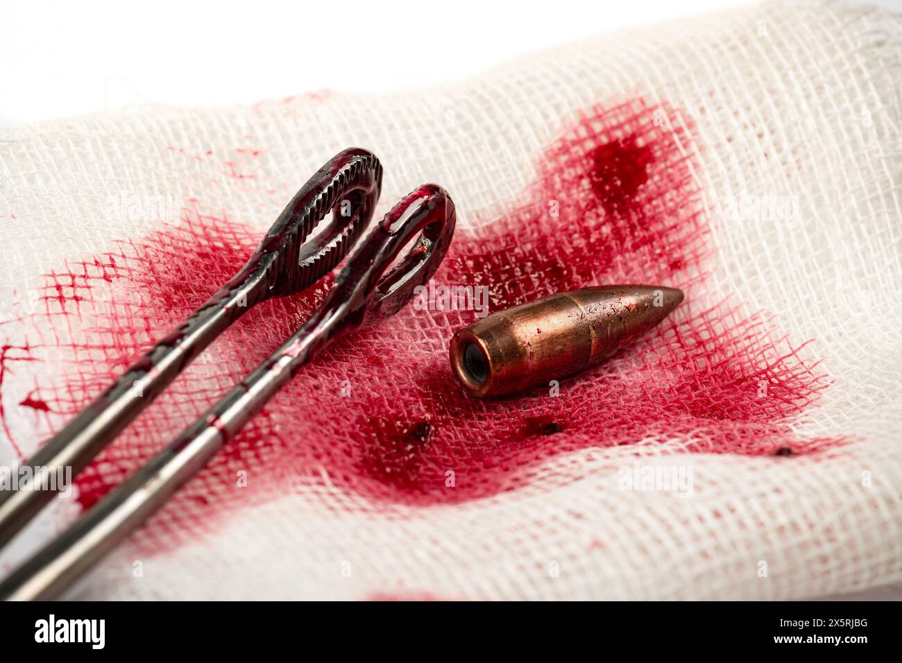 Concetto chirurgico con proiettile, pinze mediche e sangue su pezzo di bendaggio bianco Foto Stock