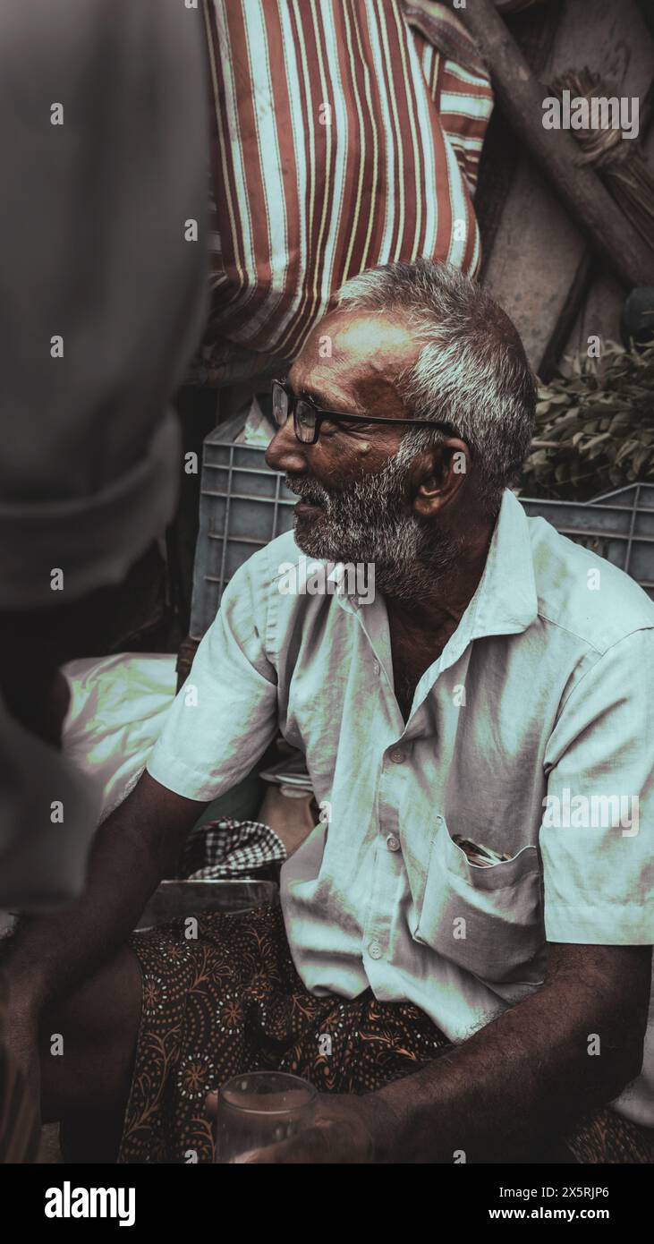 Un uomo anziano seduto accanto al suo negozio che comunica con gli altri venditori Foto Stock