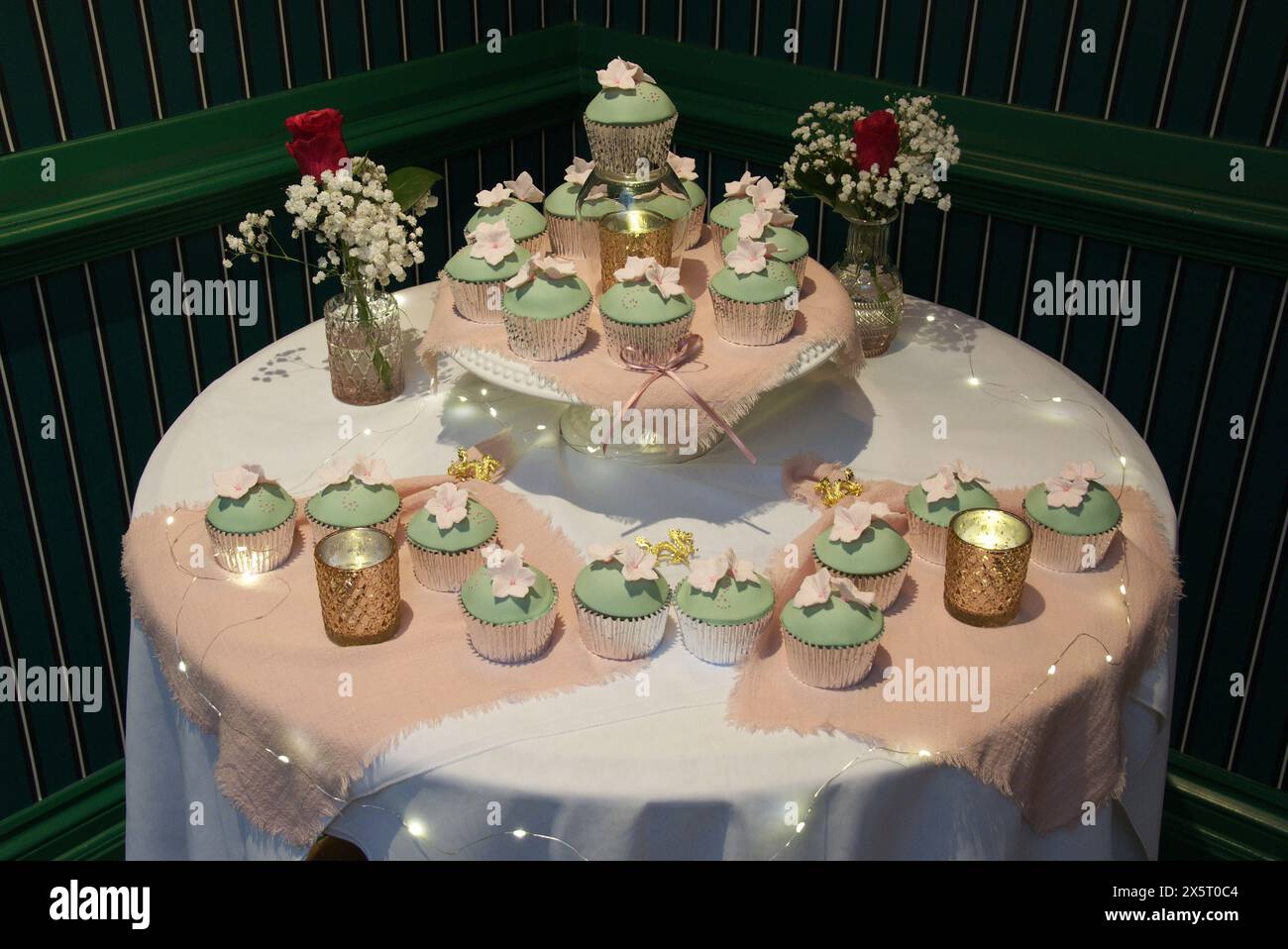Piccole torte nuziali individuali sul tavolo con fiori e luci Foto Stock