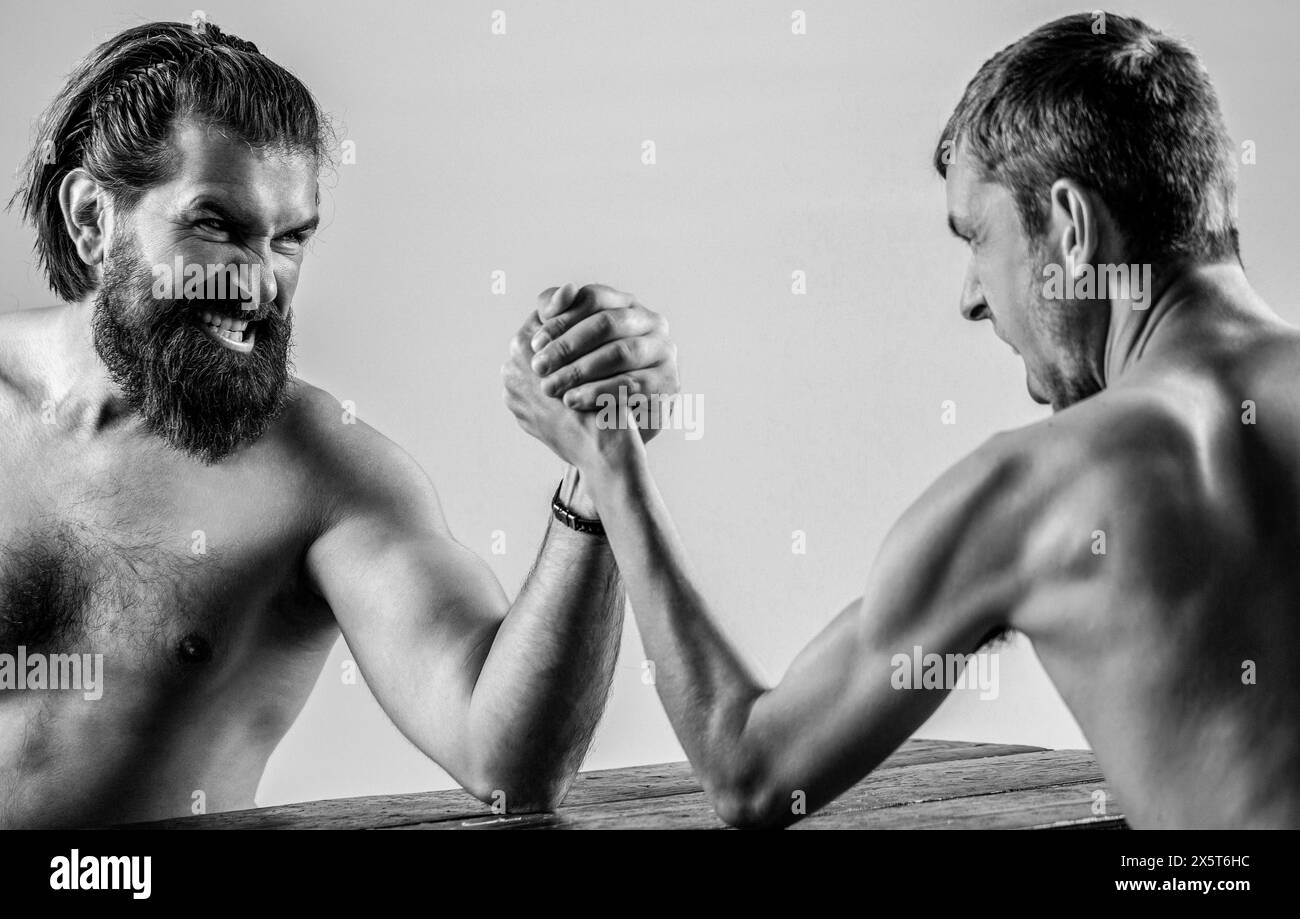 Uomo barbuto muscoloso che combatte un uomo debole e punito. Le mani di due uomini hanno stretto un braccio di lotta, forte e debole, un match ineguale. Bianco e nero Foto Stock