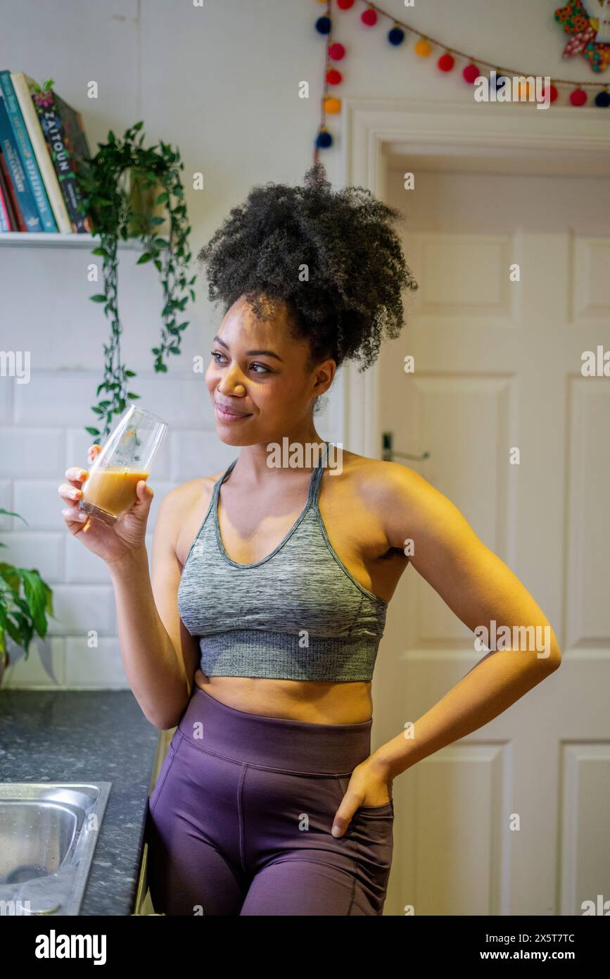 Sorridente giovane bevendo una bevanda sana a casa Foto Stock