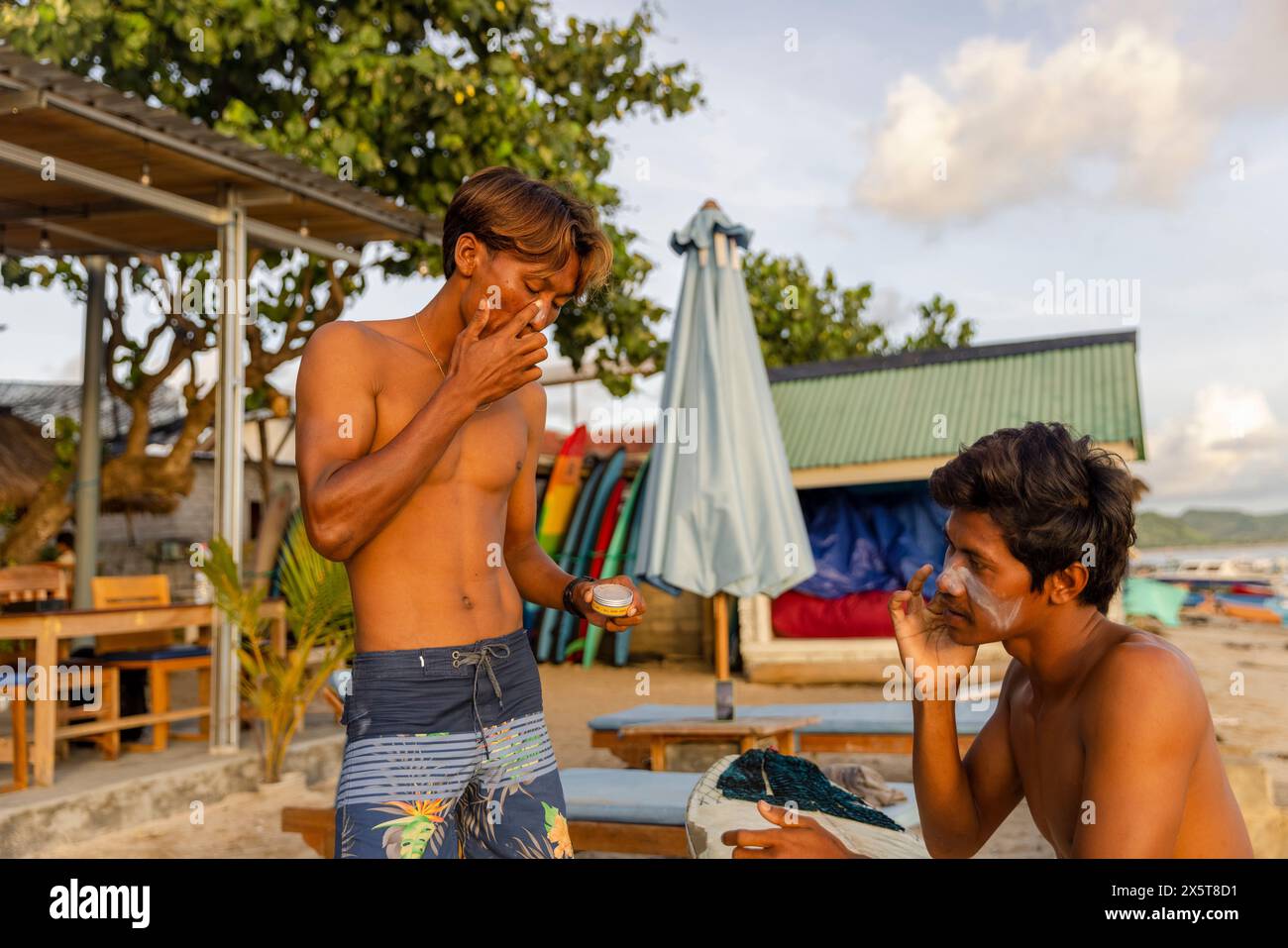 Surfista applica lozione solare sul viso in spiaggia Foto Stock
