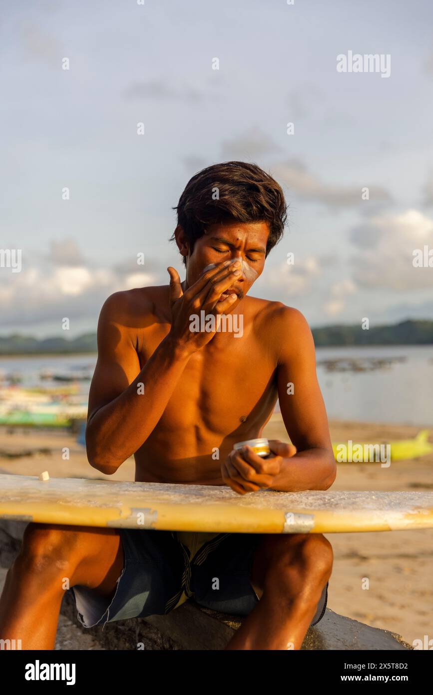 Indonesia, Lombok, surfista maschile che applica lozione solare sul viso Foto Stock