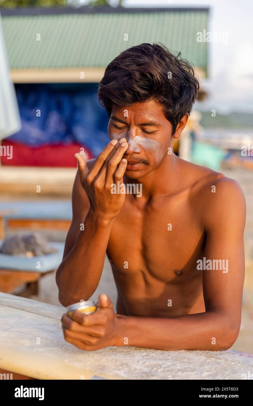 Surfista maschile che applica lozione solare sul viso Foto Stock